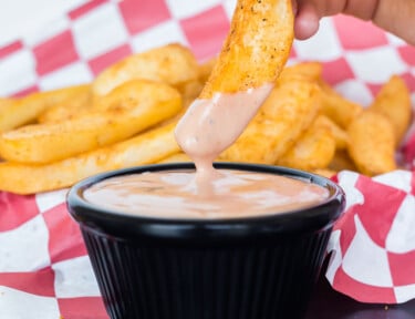 A cooked steak fry being dipped into a cup of Red Robin campfire sauce.