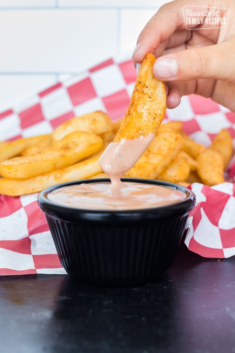 A cooked steak fry being dipped into a cup of Red Robin campfire sauce.