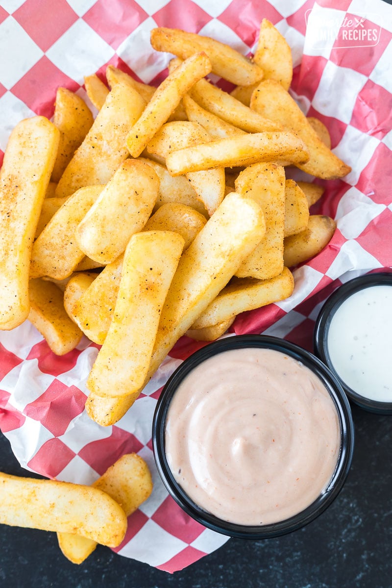 A basket of thick cut fries next to a cup of Red Robin campfire sauce and a cup of Ranch dressing