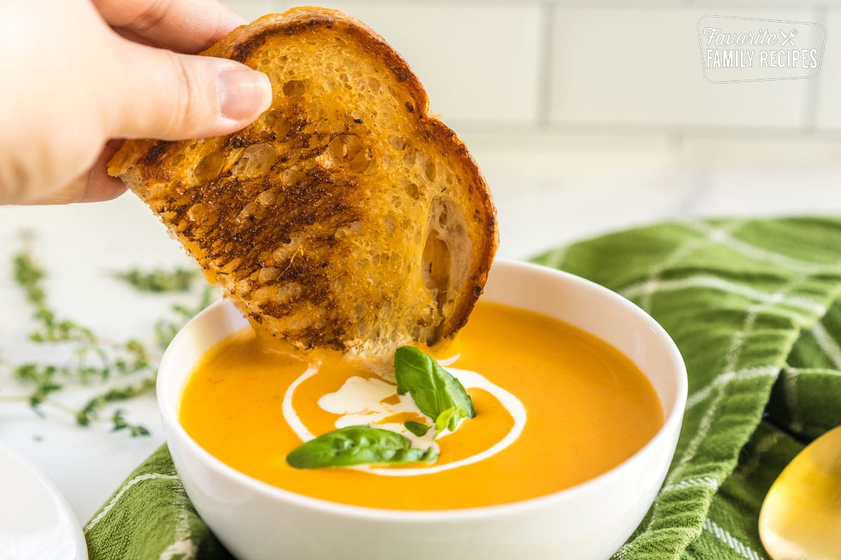 A grilled cheese sandwich being dipped in tomato soup