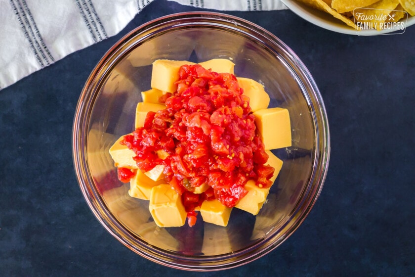 Bowl with cubes of Velveeta cheese with a can of Rotel tomatoes poured on top. Tortilla chips on the side.