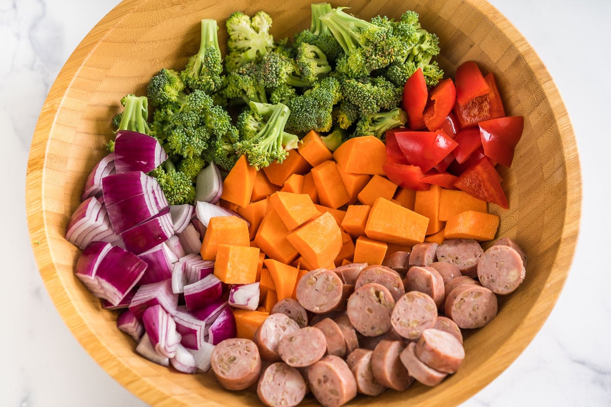 Chopped chicken sausage, red onion, red pepper, sweet potato, and broccoli in a large bowl