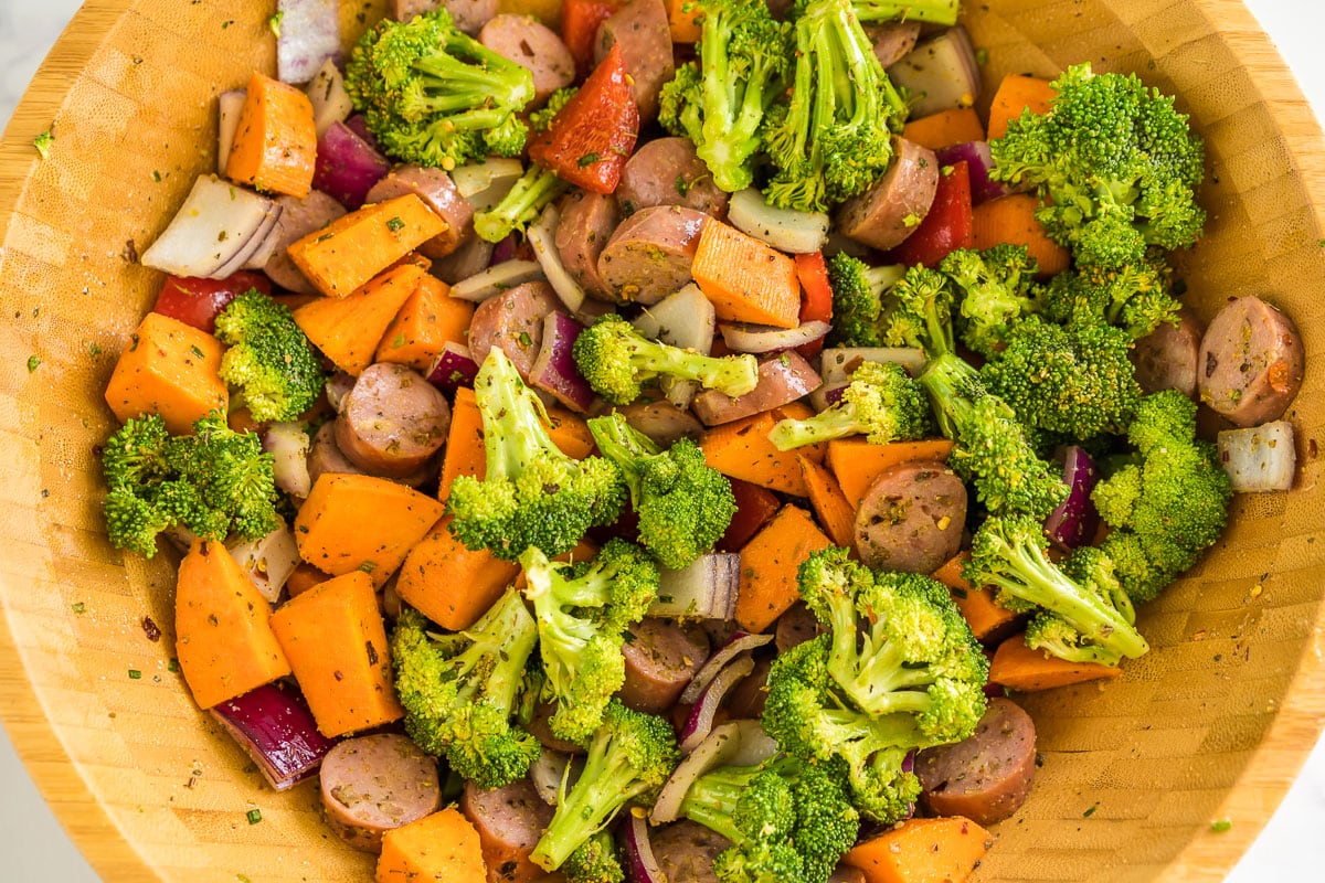 Chopped chicken sausage, red onion, red pepper, sweet potato, and broccoli tossed in olive oil and spices in a large bowl