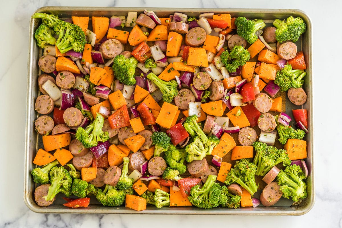 Chopped chicken sausage, red onion, red pepper, sweet potato, and broccoli tossed in olive oil and spices on a baking sheet