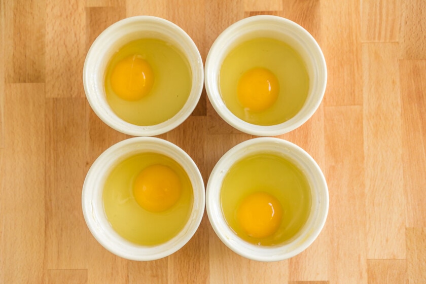 Four ramekins with an egg cracked in each one