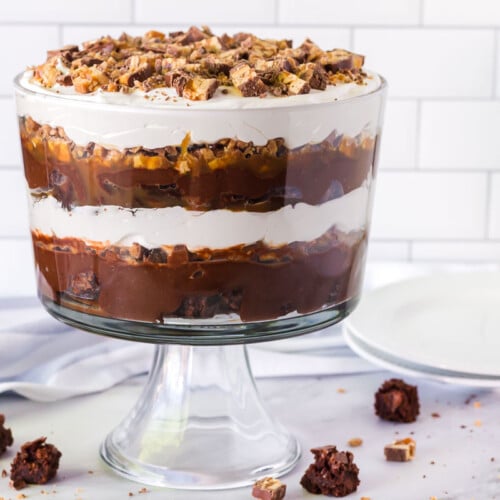 Side view of the multi layered Chocolate trifle. Serving plates on the side and brownies and Snickers are sprinkled around the table.
