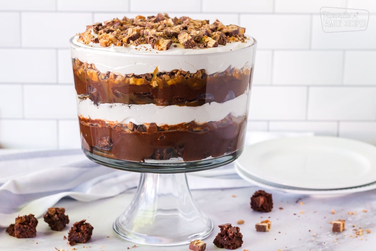 Side view of the multi layered Chocolate trifle. Serving plates on the side and brownies and Snickers are sprinkled around the table.