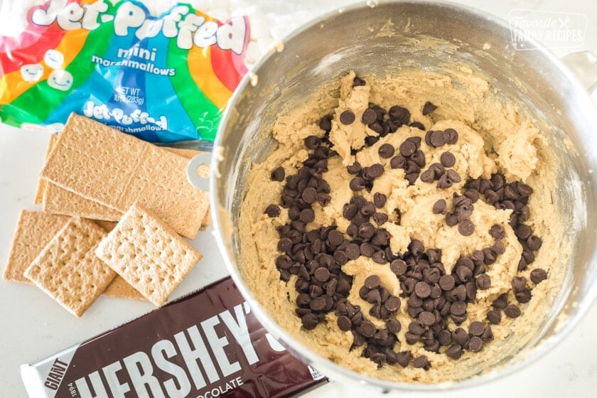 A bowl of s'mores cookie dough next to marshmallows chocolate and graham crackers