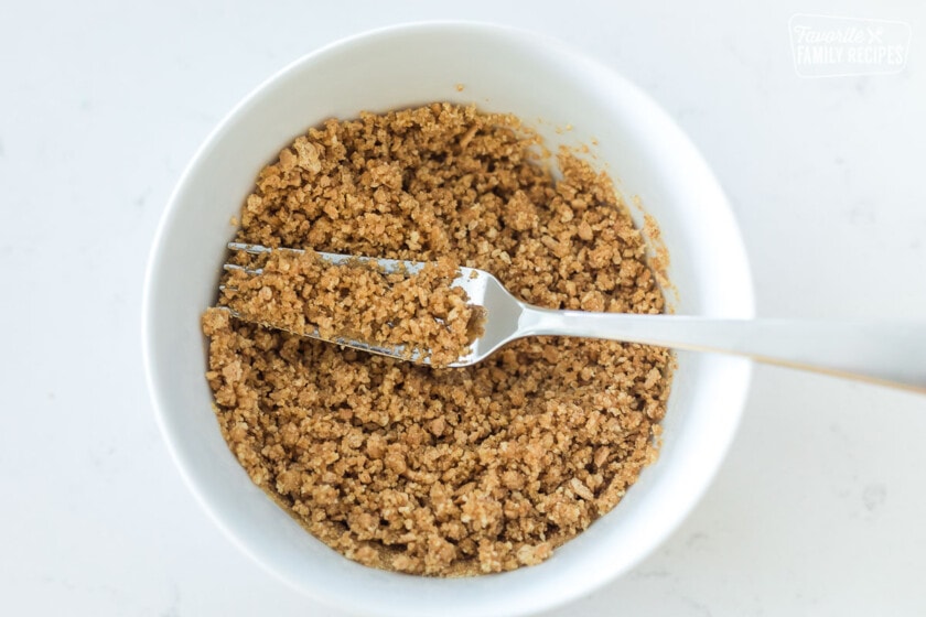 Graham cracker crumbs crumbled with melted butter in a bowl