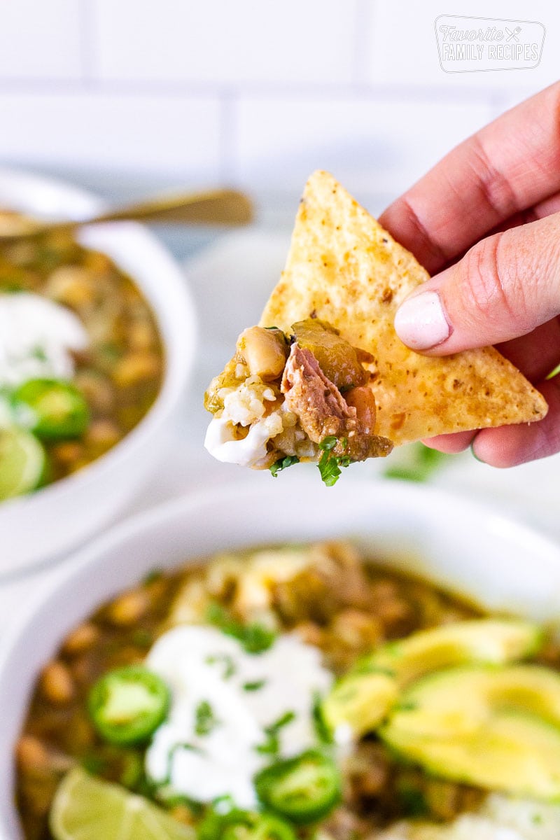 Tortilla chip with Pork Chile Verde on the corner. Bowls of Pork Chili Verde in the background.