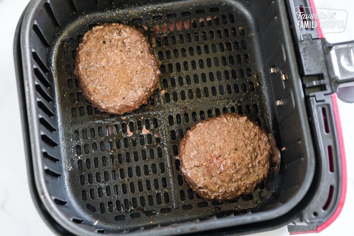 two cooked hamburger patties in an air fryer basket