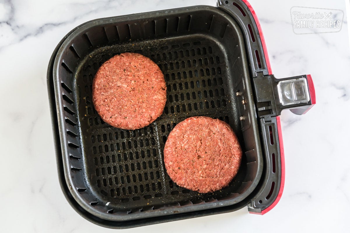 two raw hamburger patties in an air fryer basket