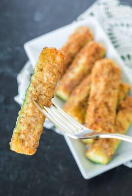 A golden brown fried zucchini spear cooked in an air fryer being held by a fork