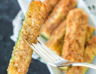 A golden brown fried zucchini spear cooked in an air fryer being held by a fork