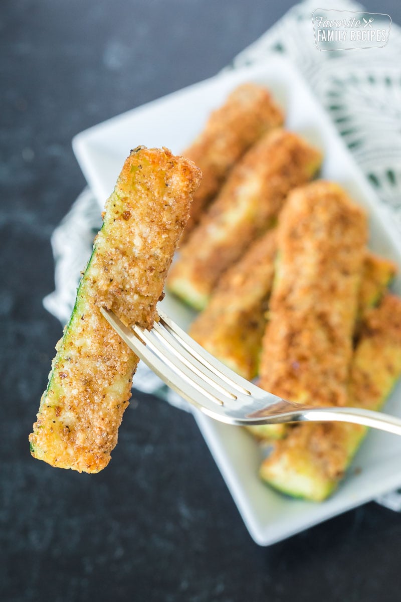 A golden brown fried zucchini spear cooked in an air fryer being held by a fork.