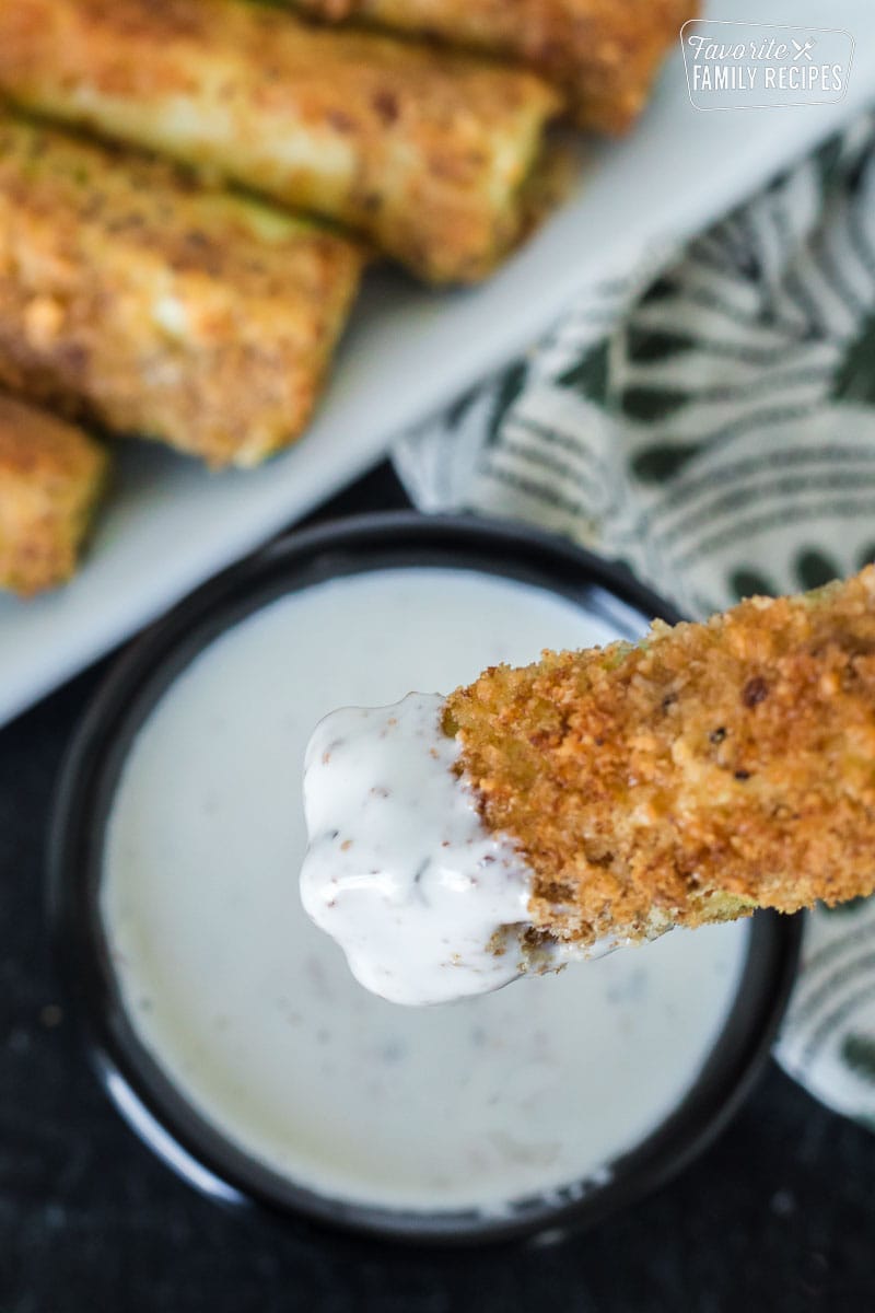 A fried zucchini spear being dipped in ranch dressing.