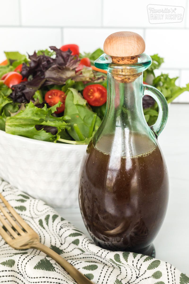 A bottle of homemade balsamic vinaigrette next to a bowl of salad