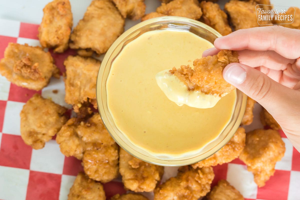 A breaded chicken nugget being dipped in Chick-Fil-A Sauce