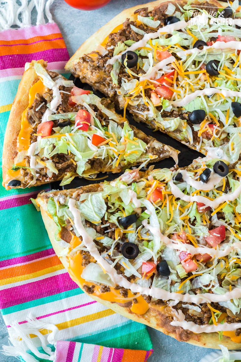 A slice of taco pizza with lettuce, tomato, ground beef, nacho cheese, and sour cream sauce.