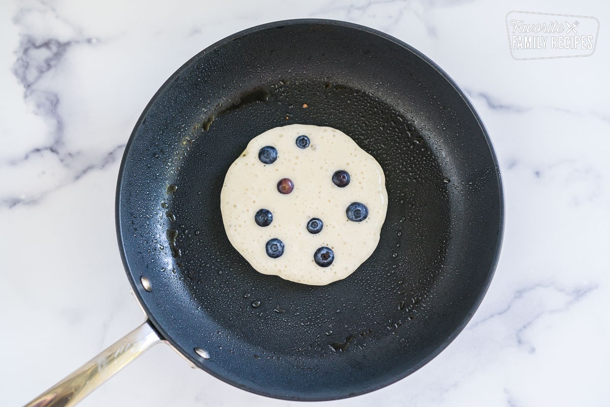 A blueberry pancake cooking on a skillet