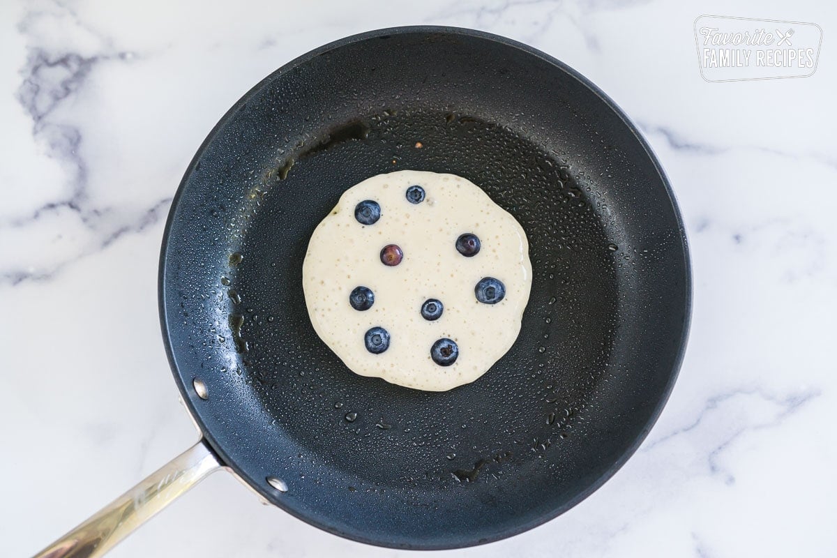 A blueberry pancake cooking on a skillet.