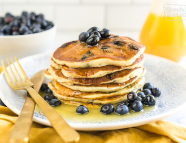 A stack of blueberry pancakes on a plate covered in syrup