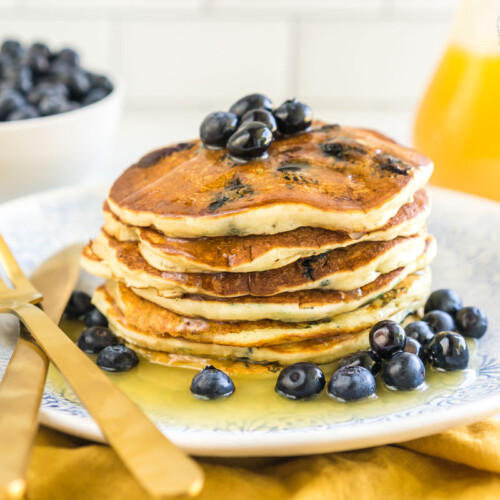 A stack of blueberry pancakes on a plate covered in syrup