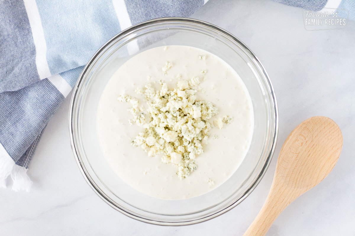 Bowl of Blue Cheese Dressing with blue cheese crumbles. Wooden spoon on the side.