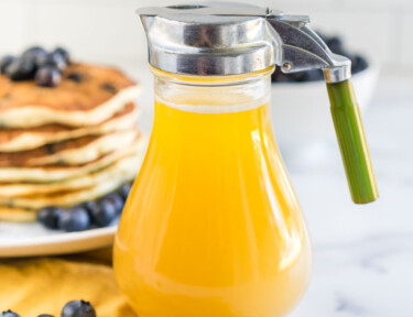 Buttermilk Syrup in a dispenser next to a stack of blueberry pancakes