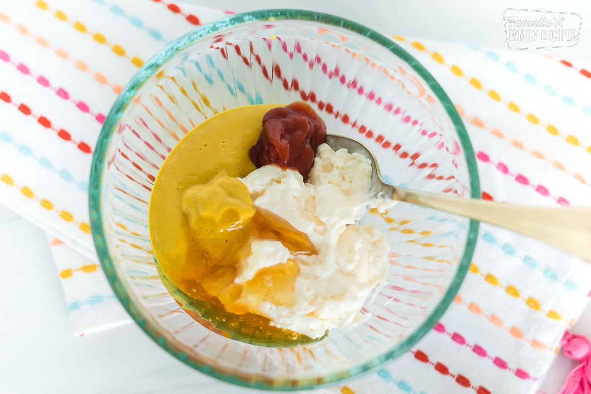 Mayonnaise, mustard, ketchup, and honey in a glass mixing bowl.