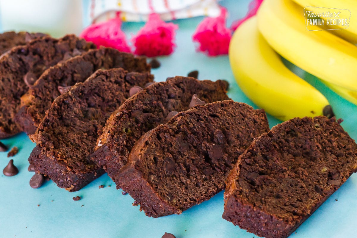 Slices of Chocolate Banana Bread fanned on a table. Yellow bananas and milk in the background.