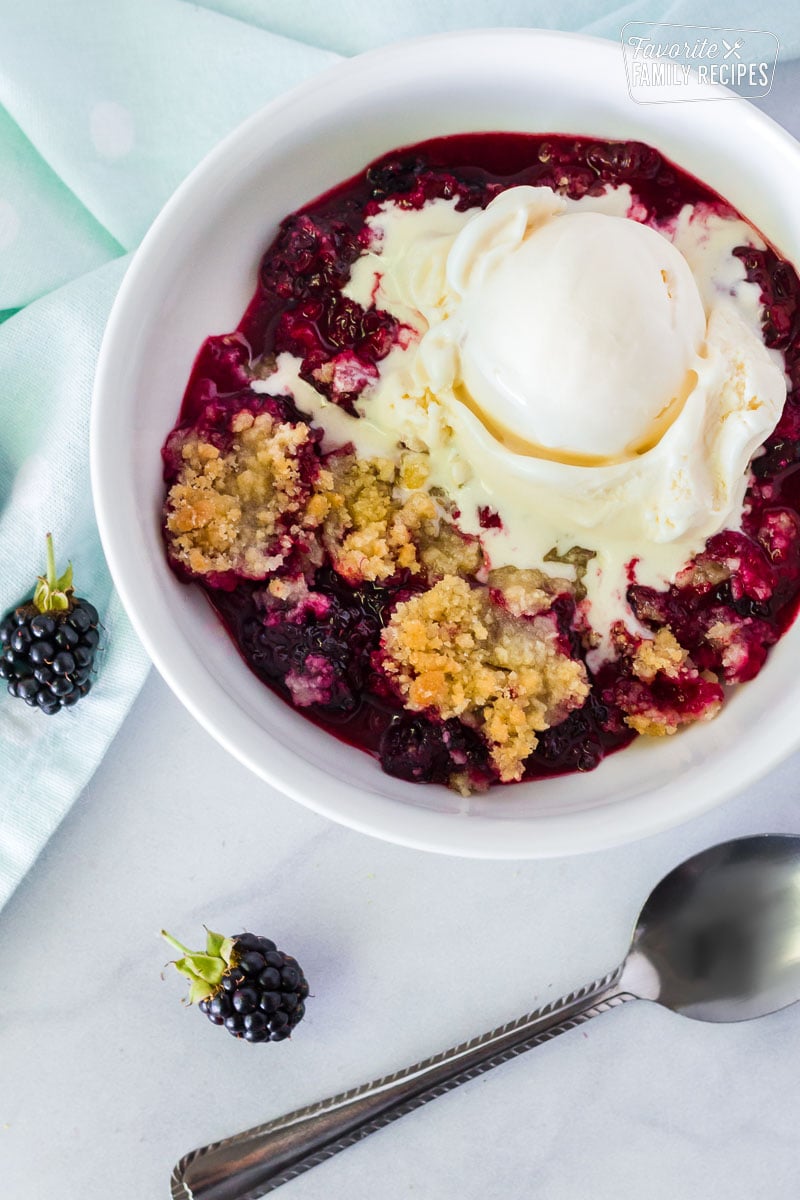 Close up bowl of Easy Blackberry Cobbler with vanilla ice cream and a spoon on the side.