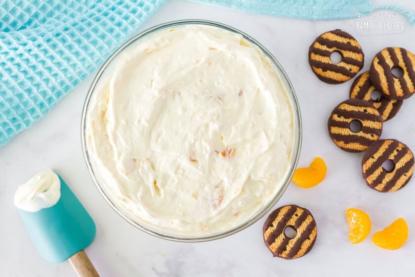 Bowl of cookie salad mix with a spatula on the side. Mandarin oranges and fudge stripes cookies on the side.