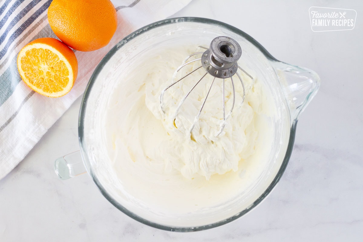 Mixing bowl of whipped heavy cream for Orange Pancake filling. Fresh oranges on the side.