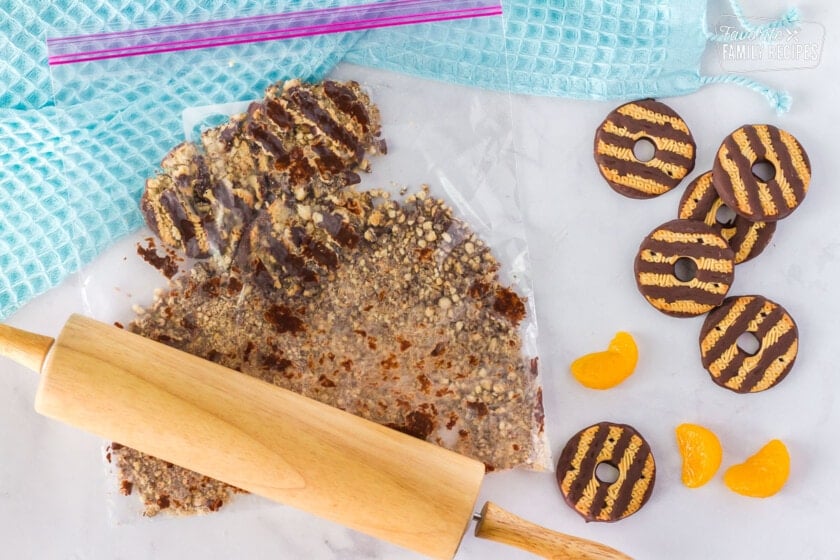 Bag of crushed fudge striped cookies with a wooden rolling pin. Mandarin oranges and fudge stripe cookies on the side.