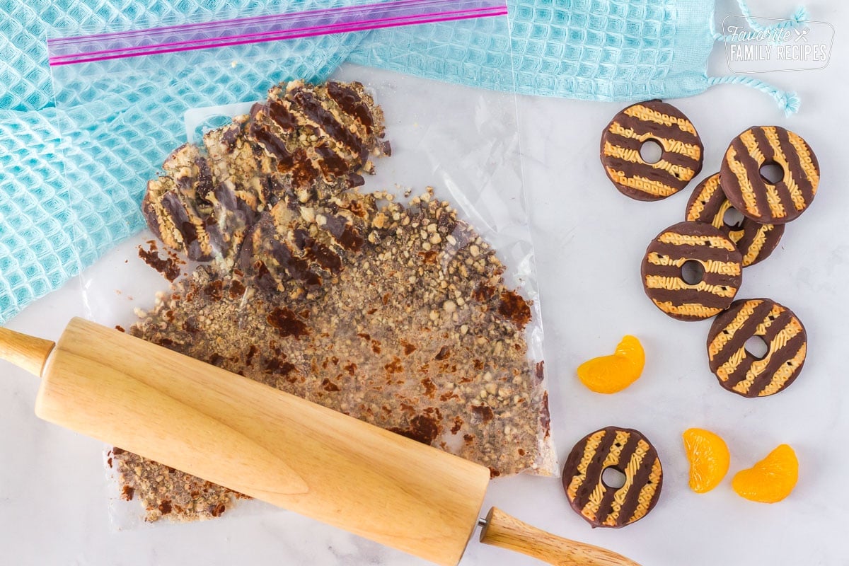 Bag of crushed fudge striped cookies with a wooden rolling pin. Mandarin oranges and fudge stripe cookies on the side.