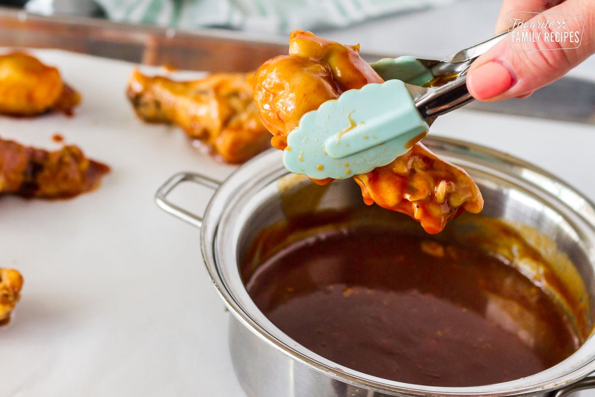 Hand holding mini tongs dipping cooked chicken wings into the sauce for Hot Wings with Blue Cheese Dressing.