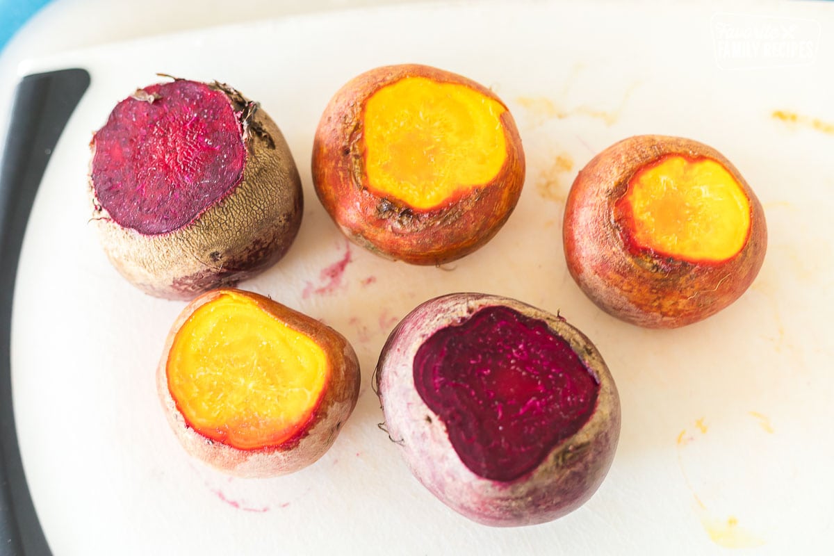 Red and golden beets on a cutting board with the tops cut off.
