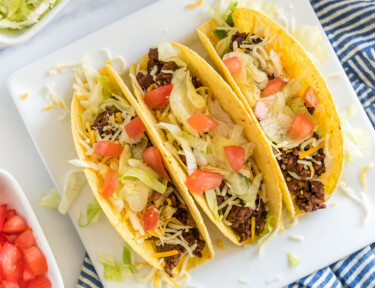Ground beef tacos with toppings on a white plate.