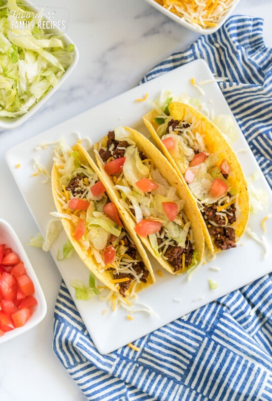 Ground beef tacos with toppings on a white plate.