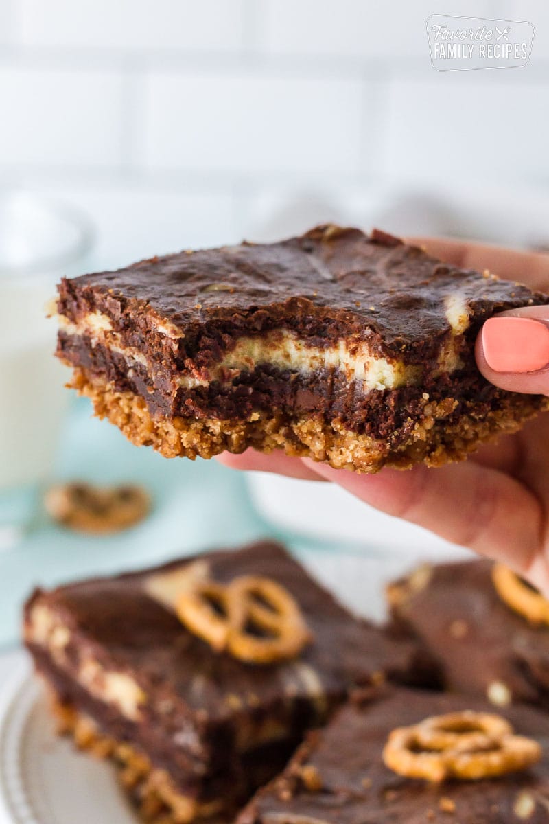 Close up of a hand holding up a Pretzel Crust Cheesecake Brownie with a bite taken out.