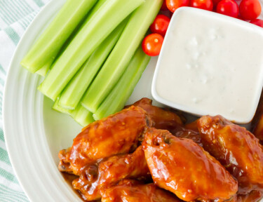 Top view of a plate of Hot Wings with Blue Cheese Dressing. Celery and tomatoes on the side.