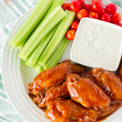 Top view of a plate of Hot Wings with Blue Cheese Dressing. Celery and tomatoes on the side.