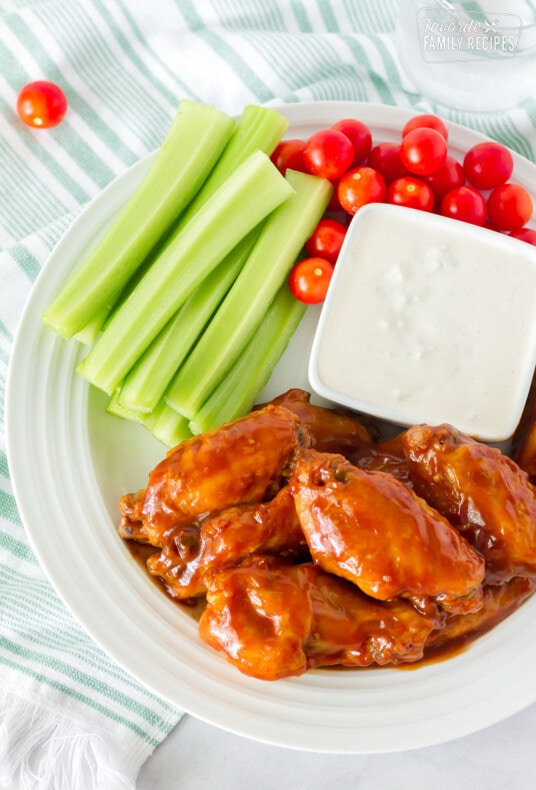 Top view of a plate of Hot Wings with Blue Cheese Dressing. Celery and tomatoes on the side.