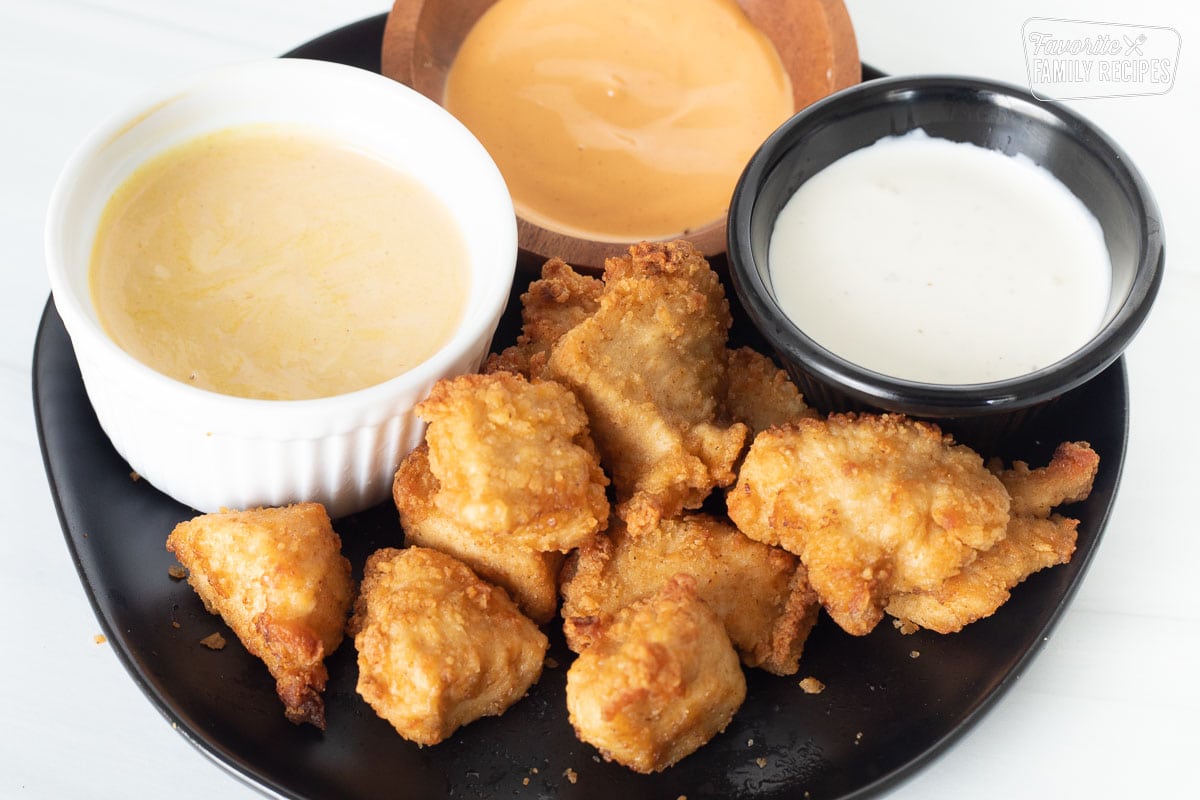 Cooked chicken nuggets on a plate with three dipping sauces.