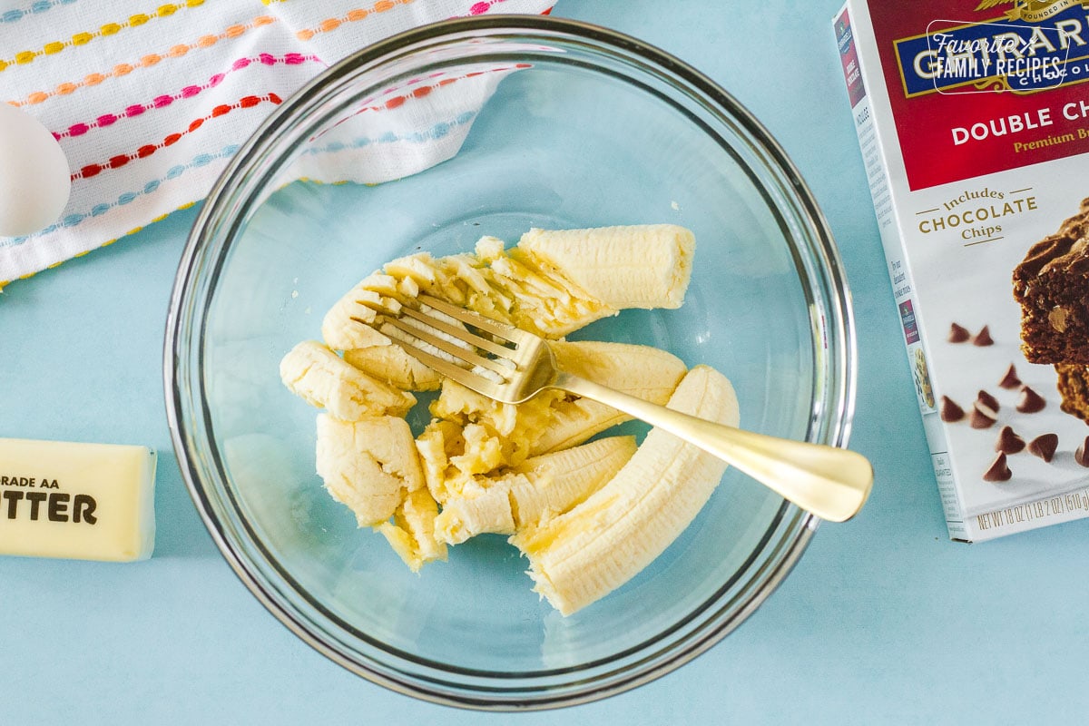 Glass bowl with fork mashing bananas.