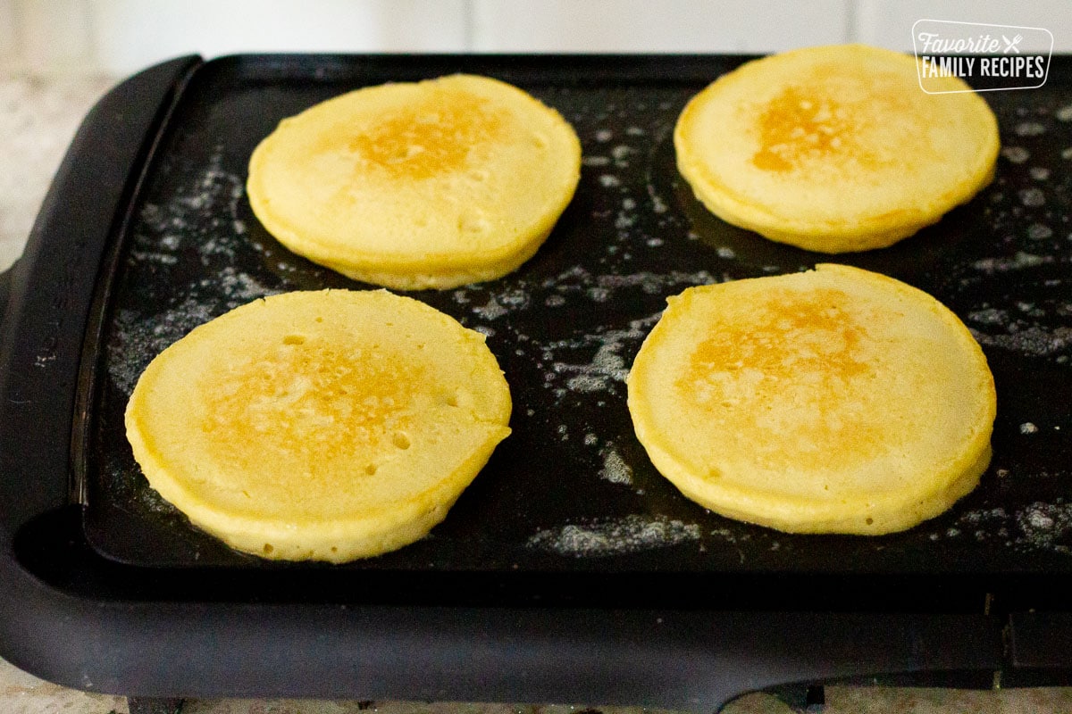 Four orange pancakes cooking on a griddle.