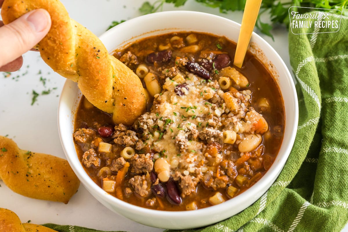 A breadstick being dipped in pasta e fagioli soup.