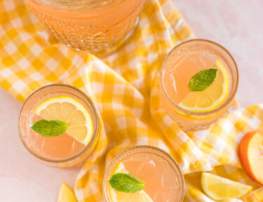Three glasses of peach lemonade topped with lemon slices and mint leaves