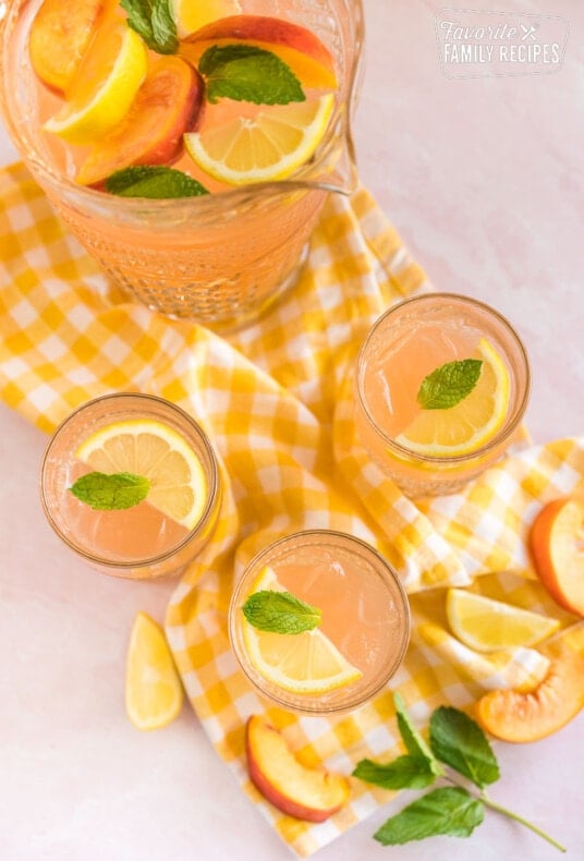 Three glasses of peach lemonade topped with lemon slices and mint leaves